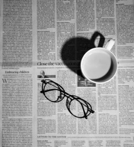 A coffee mug and pair of reading glasses on top on a newspaper.