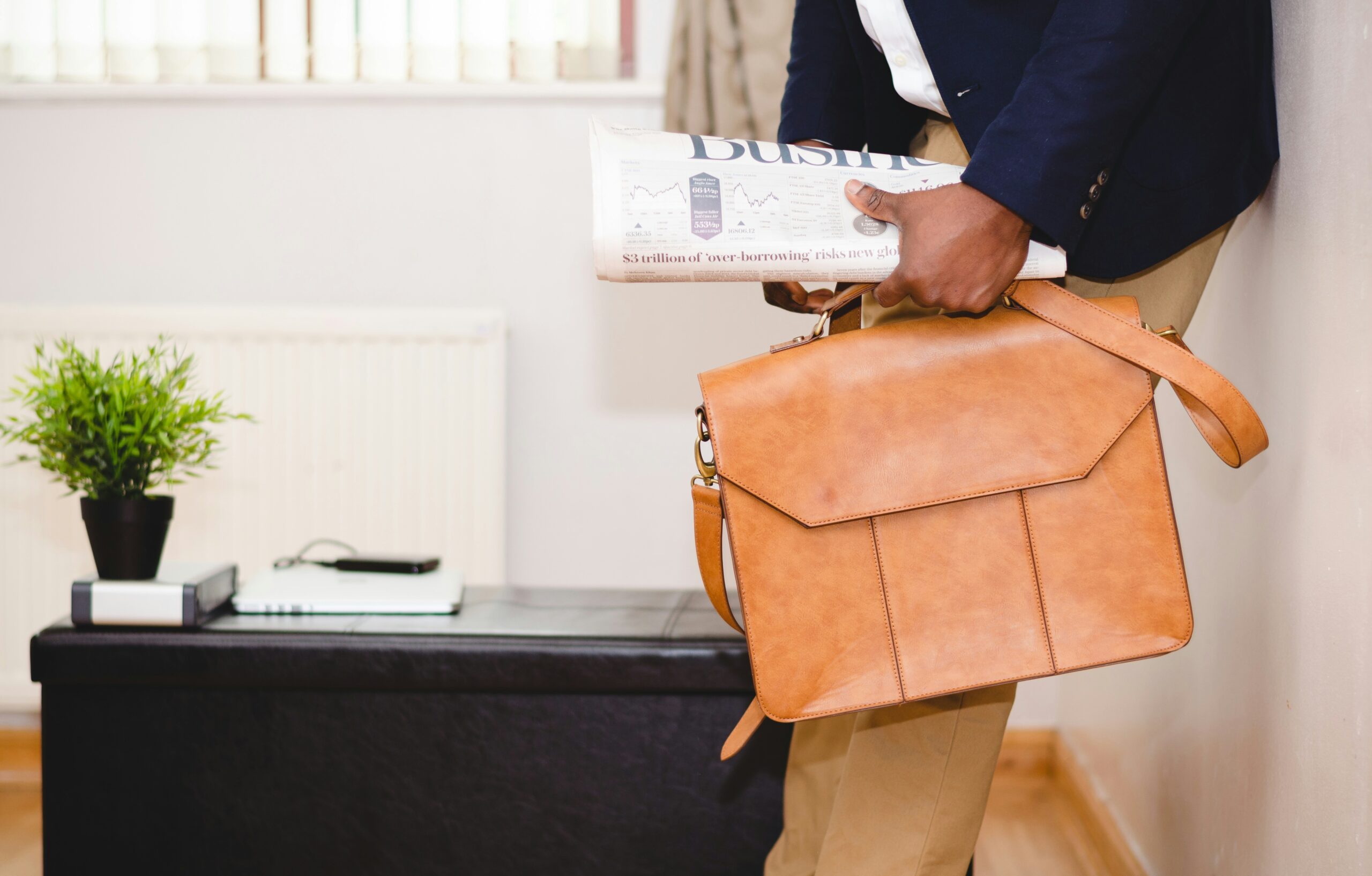 A person walking into an office setting carrying a briefcase and a newspaper.